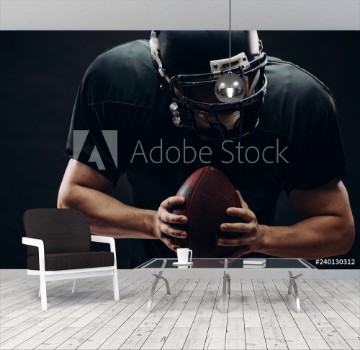 Picture of American football player with black helmet and armour running in motion holding ball getting ready to score a goal close up shot over dark background
